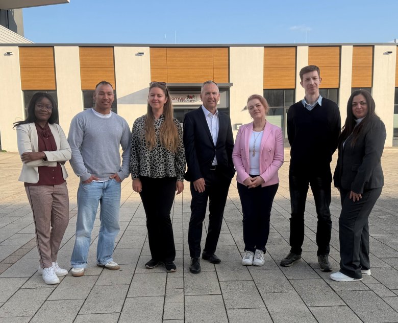 Sieben Personen aus verschiedenen Nationen stehen zusammen auf einem Stadtplatz