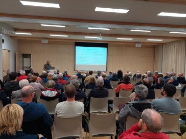 Mehrere Personen sitzend in einem Saal auf eine Leinwand schauend