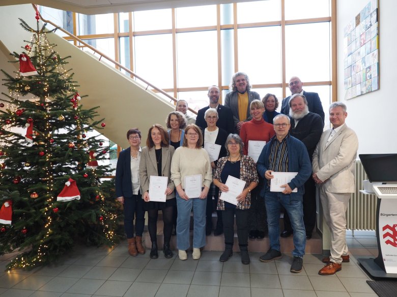 Mehrere Personen stehend vor einer Treppe mit Zertifikaten haltend