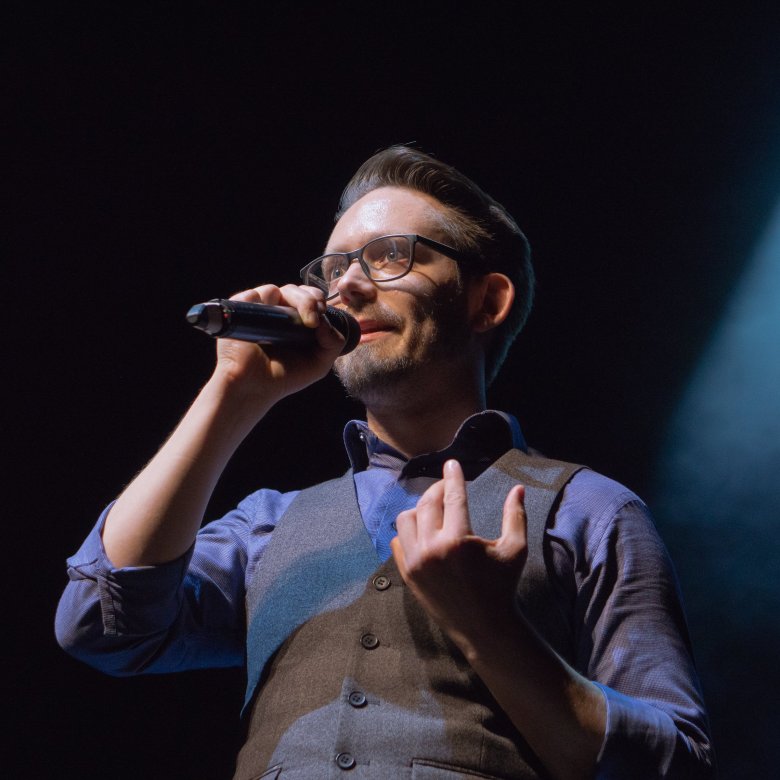 Mann mit Brille und blauem Hemd auf einer Bühne